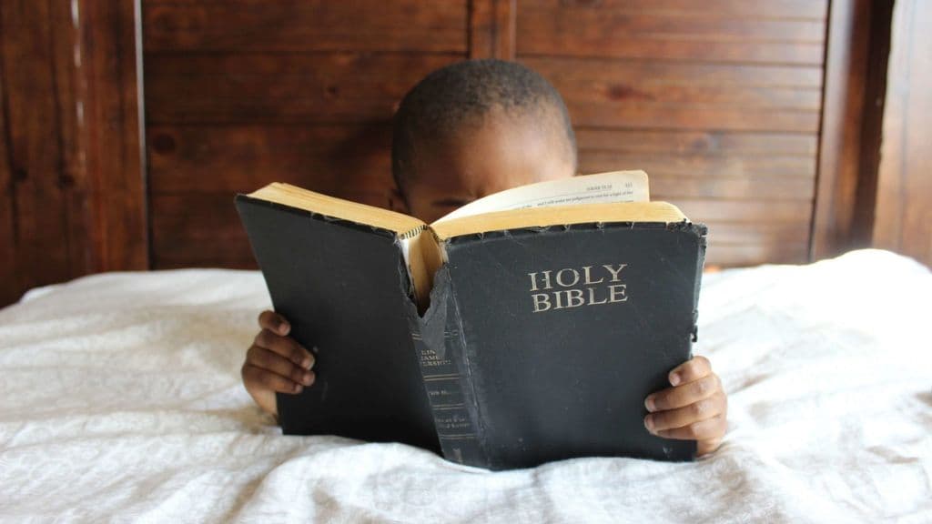 menino lendo a bíblia na cama