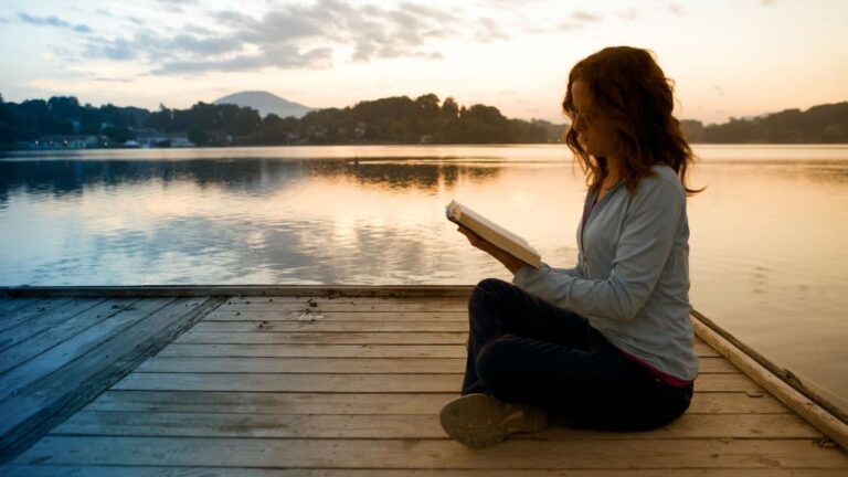 mulher lendo a bíblia sentada a beira do rio